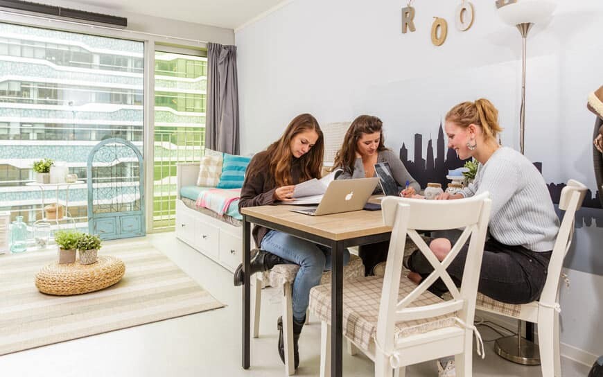 three students in a room with big windows